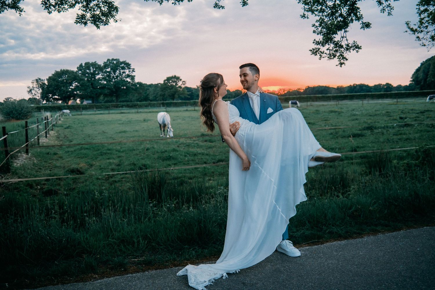 A romantic sunset wedding photo shows a couple in formal attire on a country road with a horse grazing in the background.