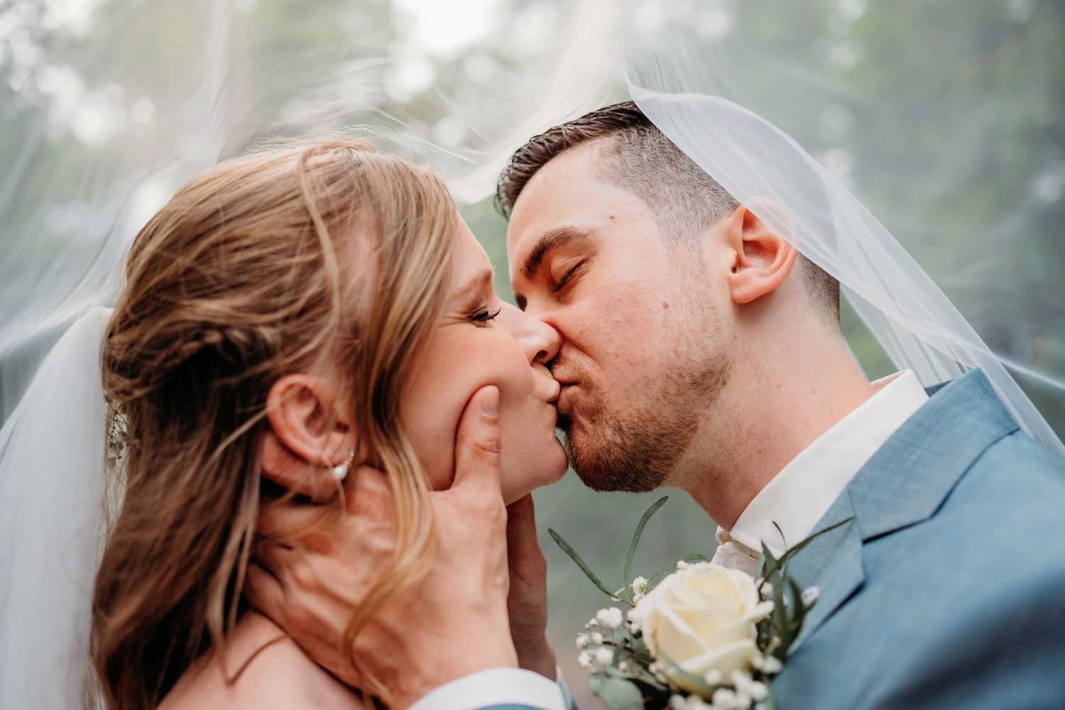 Romantic wedding couple sharing an intimate kiss while holding a white rose boutonniere.