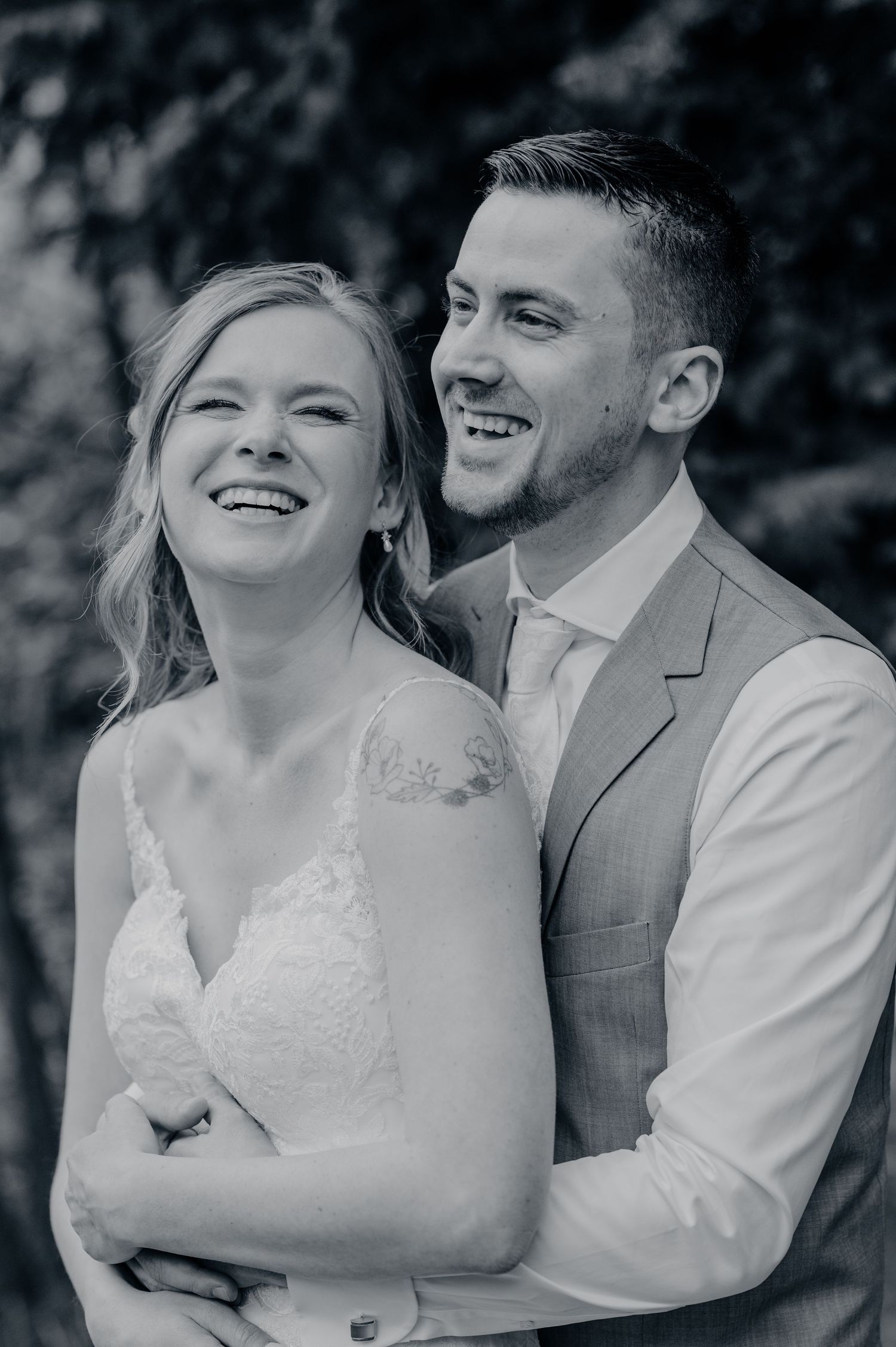 A joyful black and white wedding portrait captures a couple sharing a candid moment of laughter together.