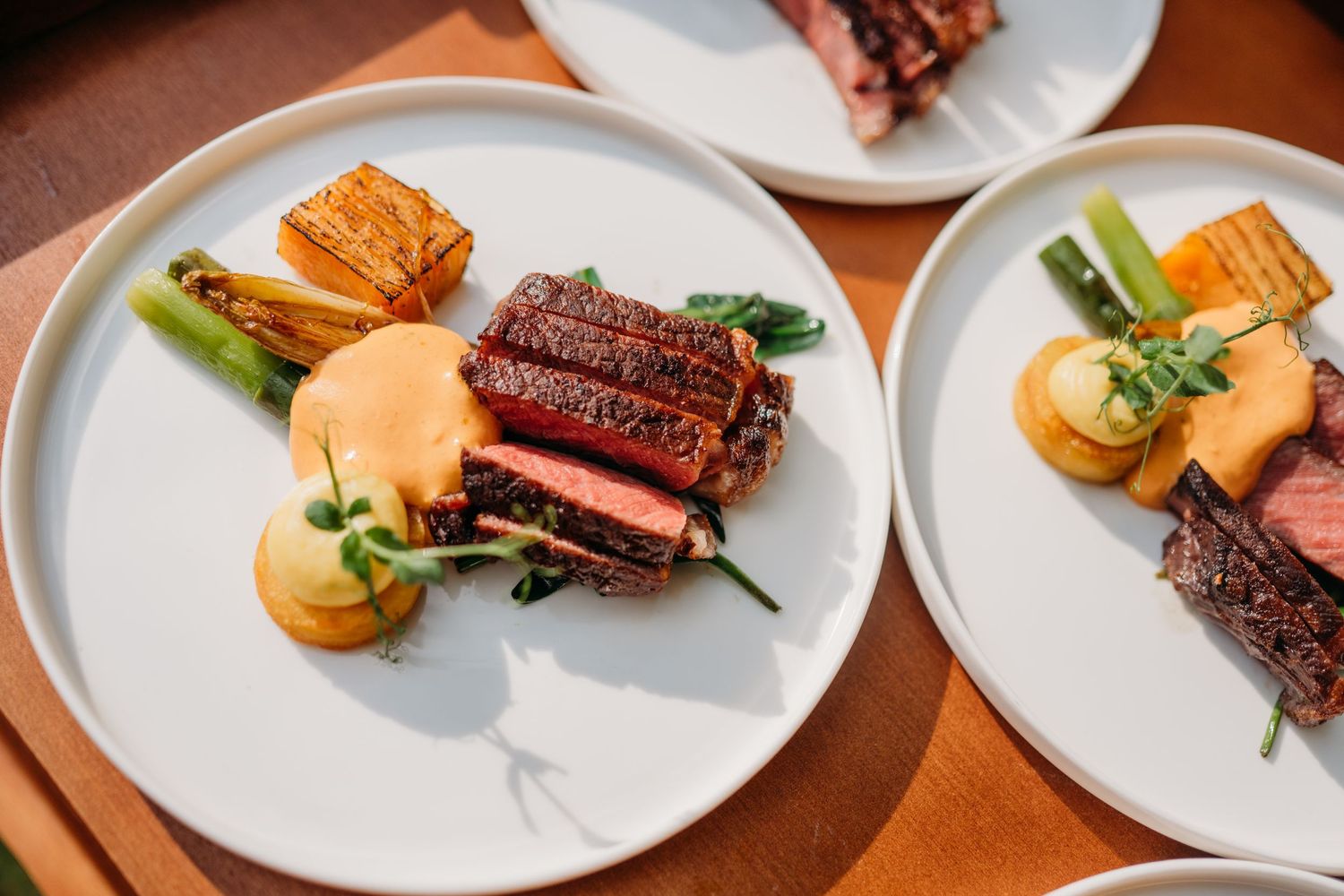 Elegant plated meal featuring seared steak, golden buns, and fresh vegetables served on white plates.
