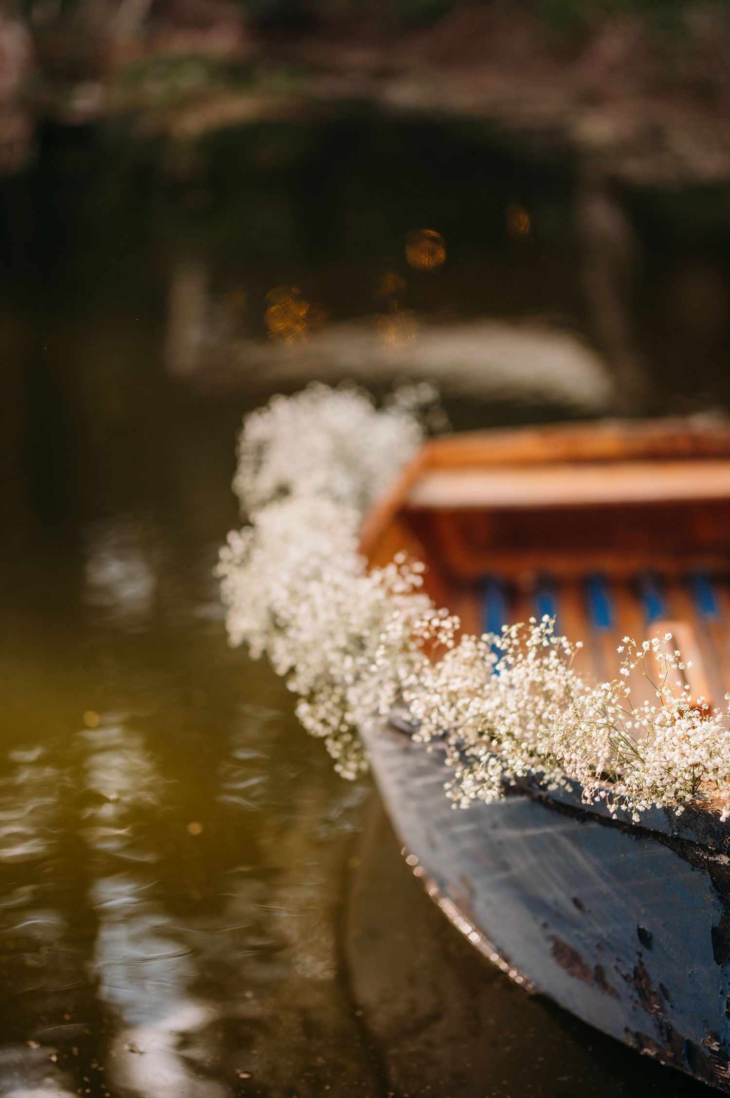 Delicate white baby's breath flowers cascade over the edge of a wooden boat floating on dark water.
