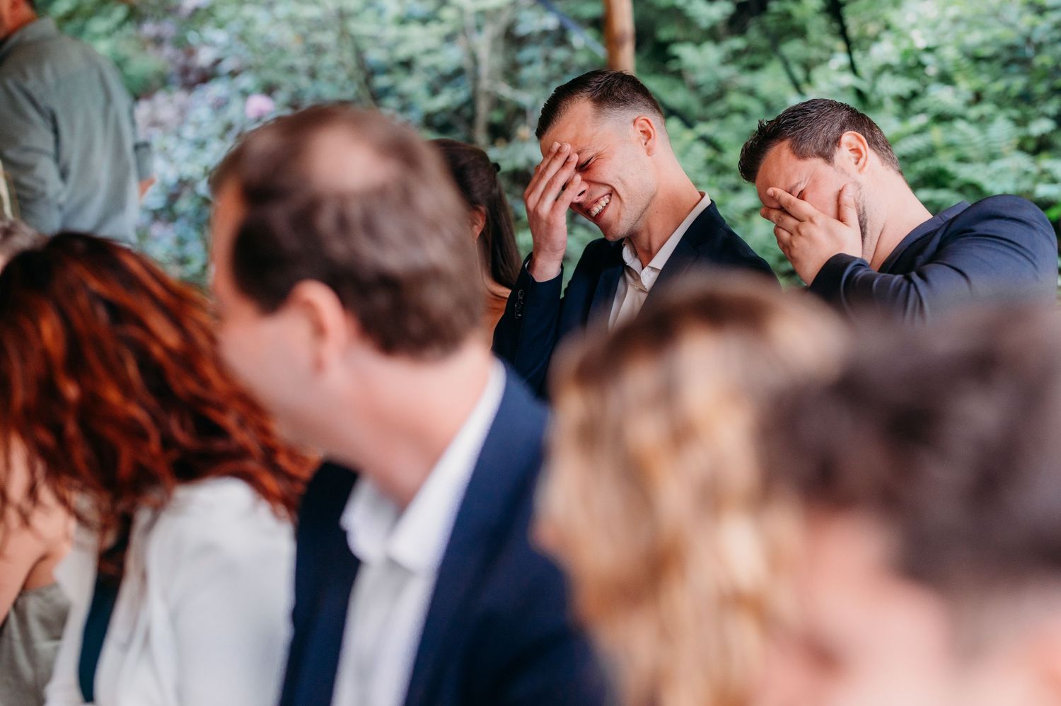 A candid moment of laughter shared during a wedding ceremony in an outdoor forest setting.