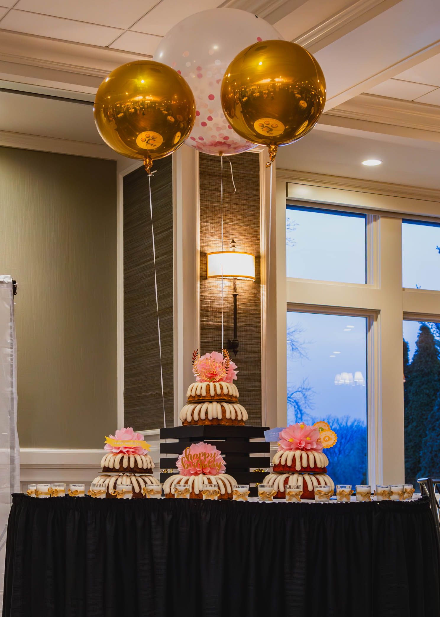 Elegant display of bundt cakes with gold balloons at graduation celebration.