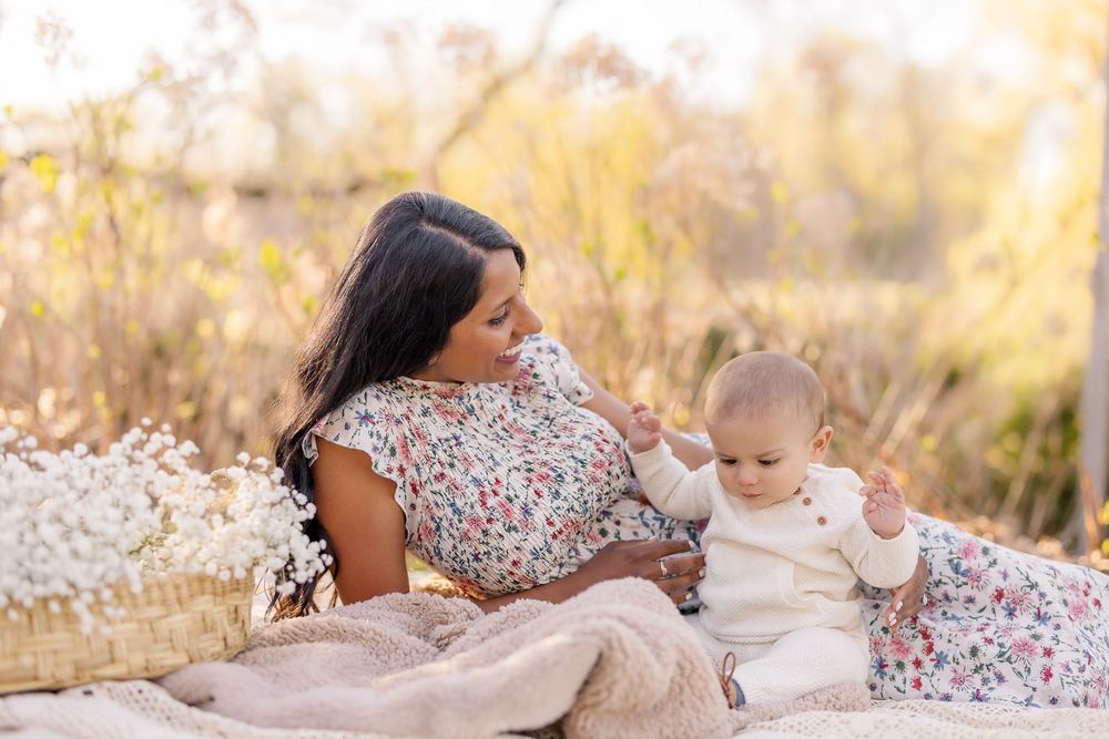 A tender moment shared on a picnic blanket in a sunlit field with tall grass and floral dresses.