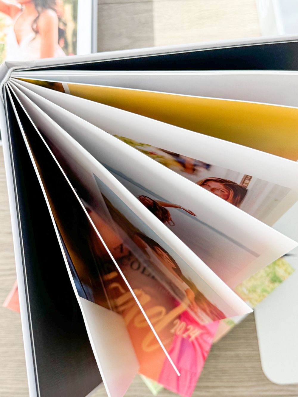 Close-up view of fanned out photo album pages showing glimpses of photographs between white and gold colored pages.