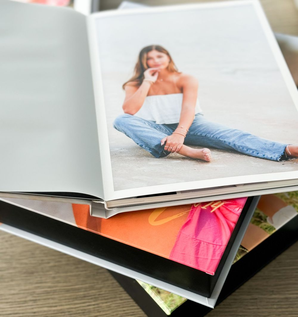 A stack of glossy photo albums or printed photographs lies open on a wooden surface showing fashion and portrait images.