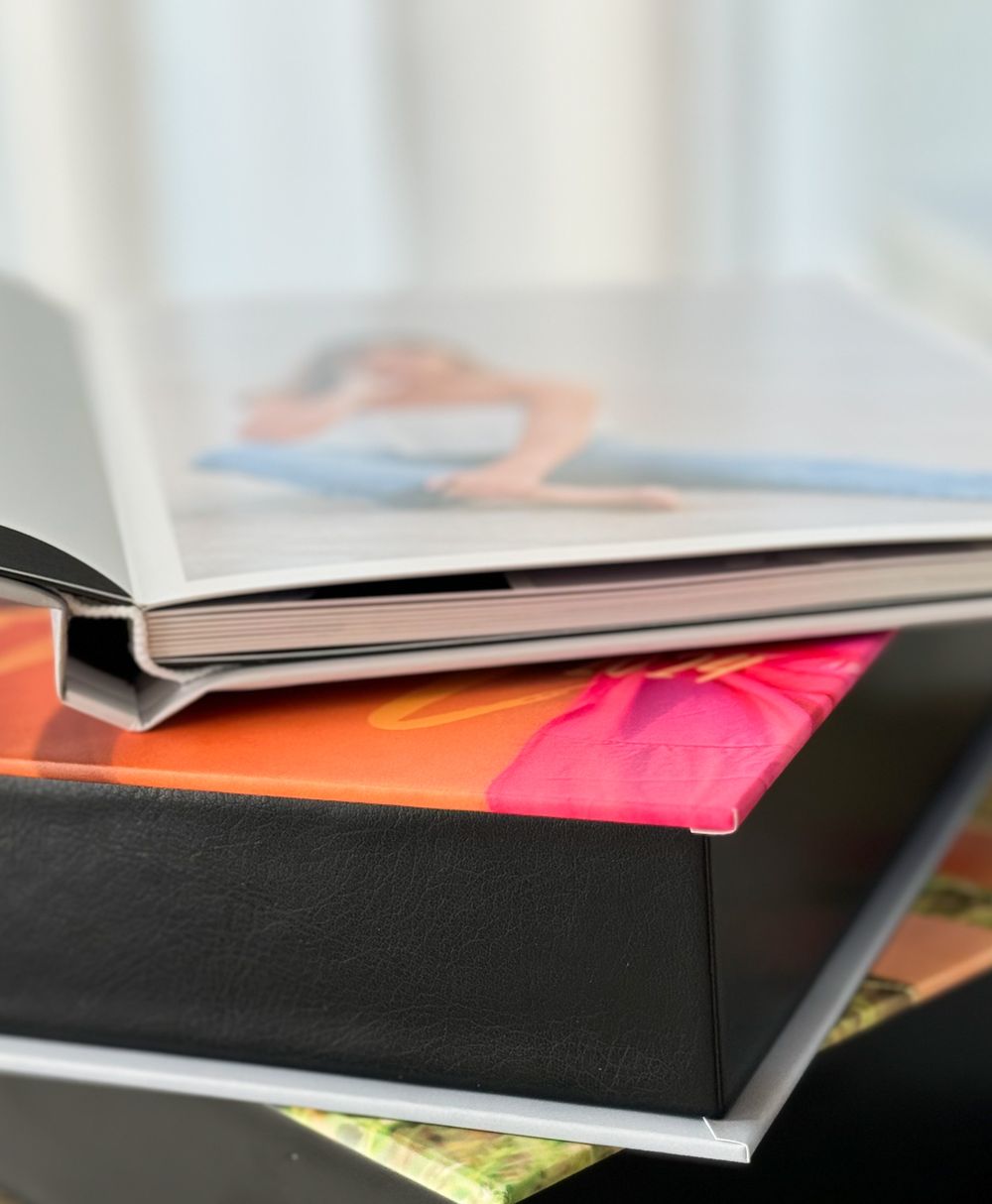 A stack of hardcover books and folders displaying colorful pages and papers in orange, pink, and black tones.