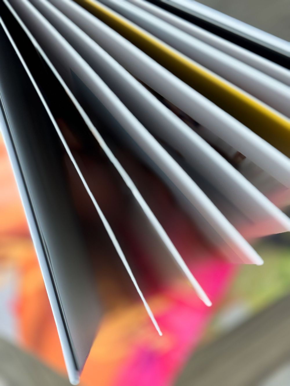 Close-up view of fanned out paper or book pages showing colorful blurred edges against a soft background.