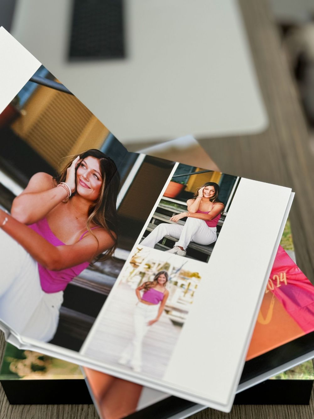 An open photo album displaying pink themed photoshoot images lies on a wooden surface.