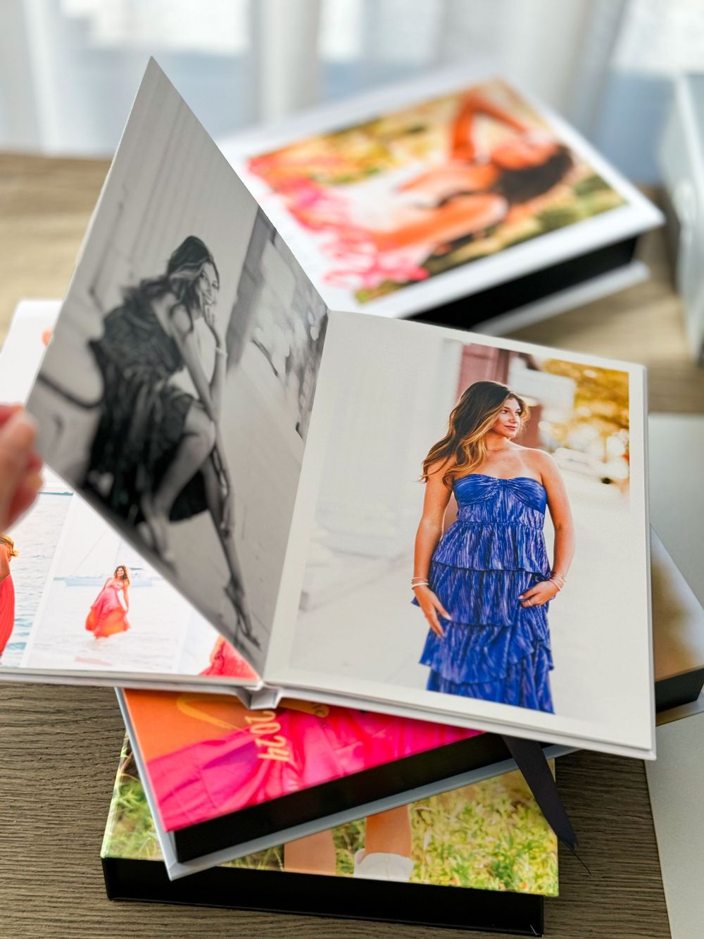 Stack of open photo albums showing fashion portraits and photography prints on wooden table.