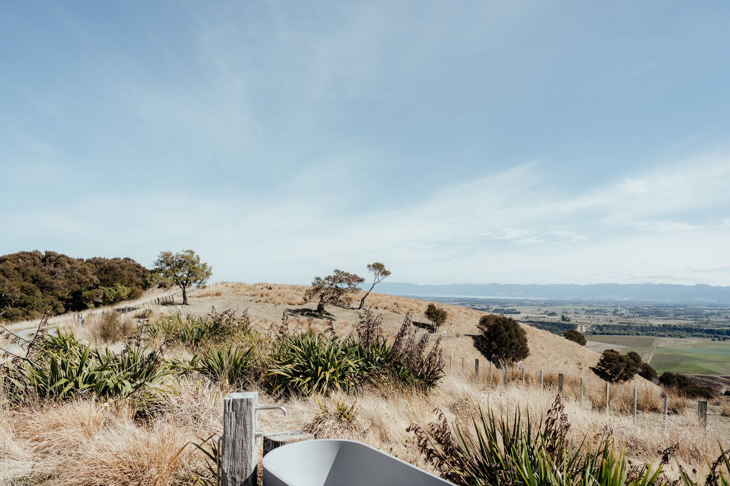 A scenic hilltop overlook with native grasses offering panoramic views of the valley and mountains beyond at Whitimanuka by August and Vine