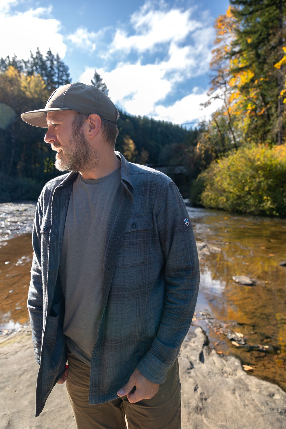 Person in casual attire standing by autumn riverside with colorful foliage.