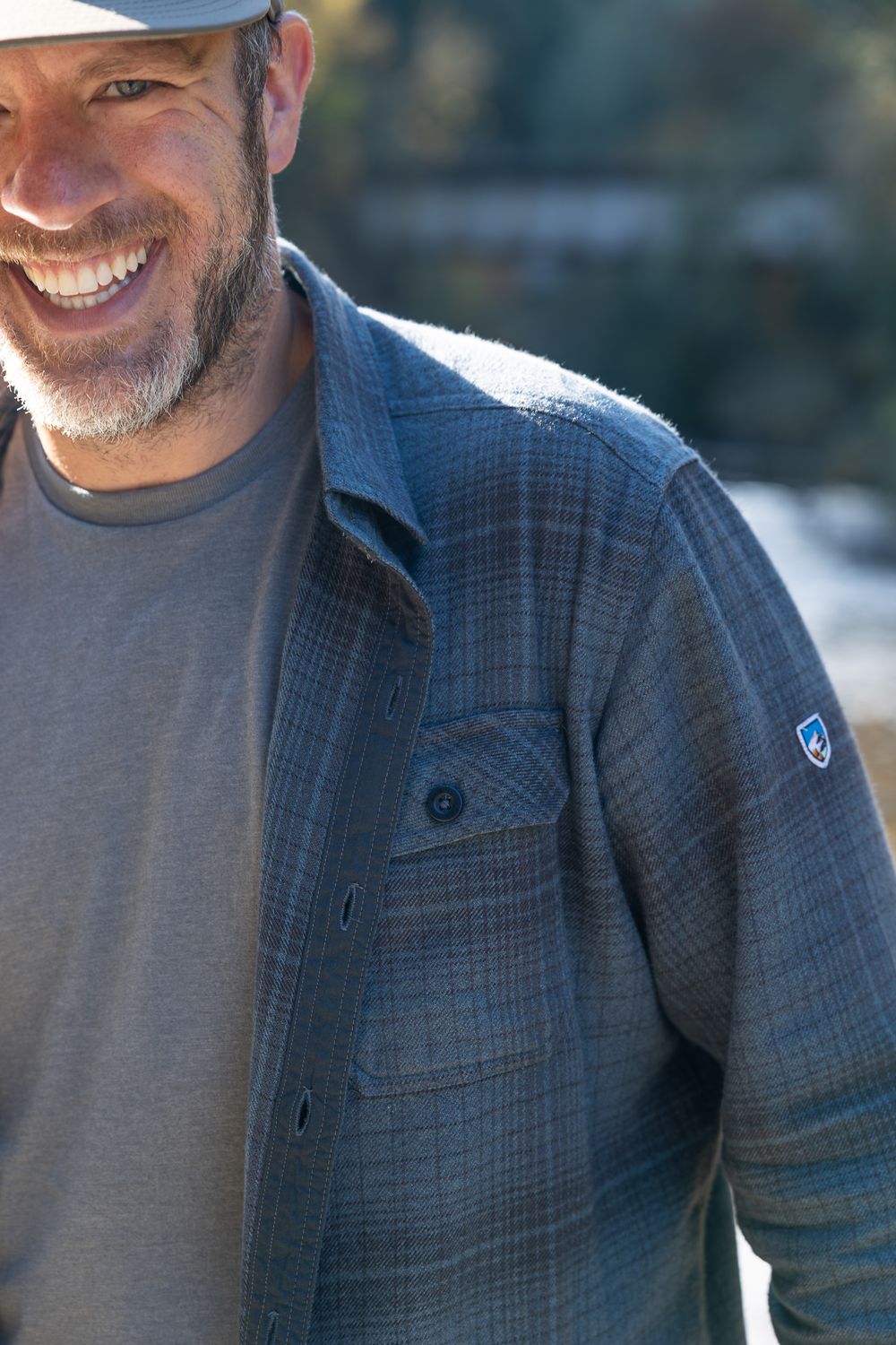 Close-up of blue plaid outdoor shirt with logo detail in natural lighting.