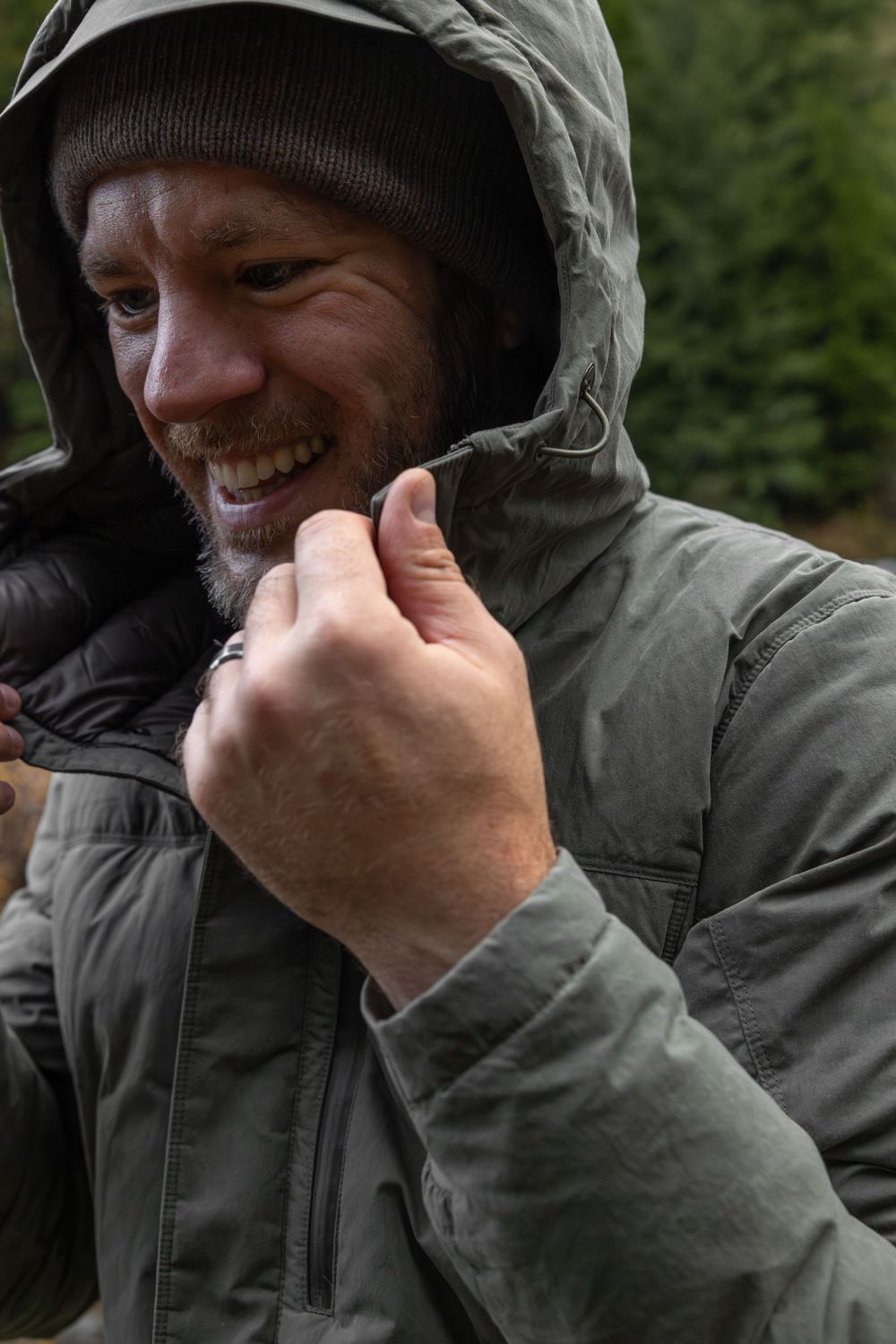 Person in a hooded jacket laughs while adjusting the zipper outdoors.