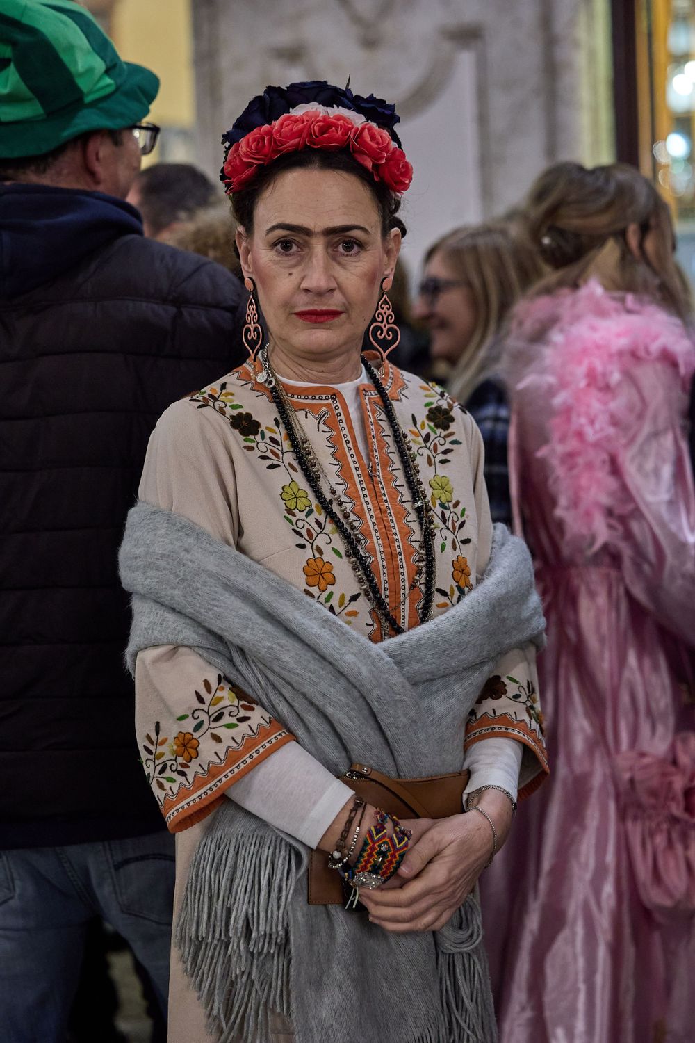 A woman wearing traditional Mexican-inspired clothing with red floral headpiece, embroidered dress and gray shawl at an event.