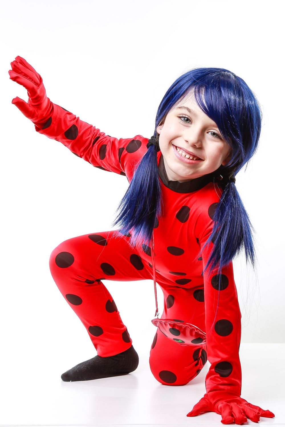 Person in red and black polka dot costume with blue hair posing playfully against white background.