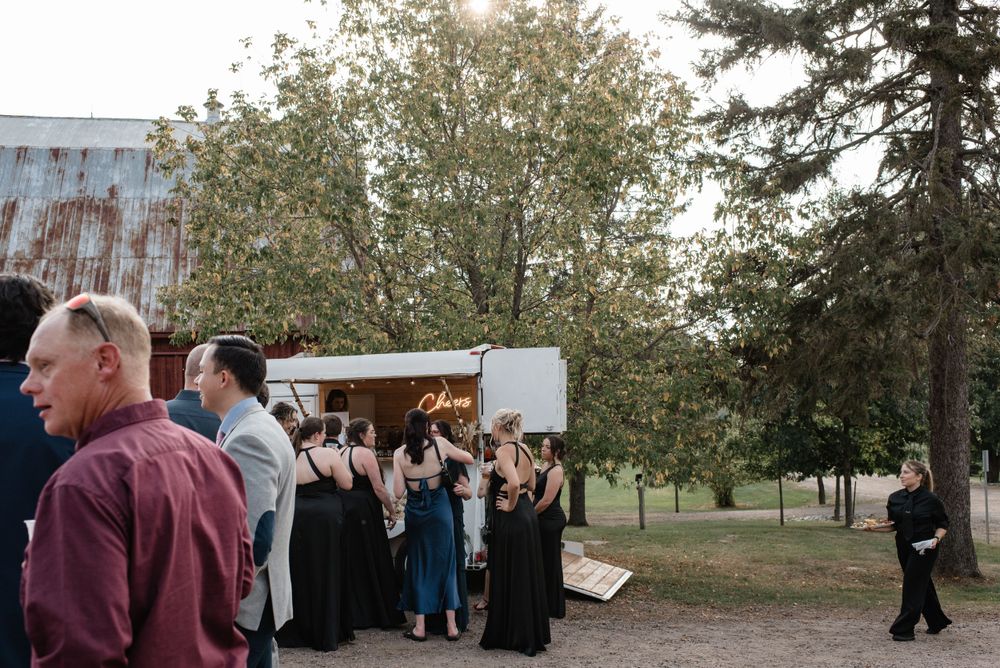 Evening wedding reception outside vintage barn with guests socializing near food truck.