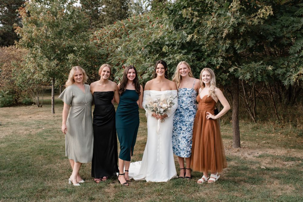 A group in formal attire stands together outdoors, wearing elegant dresses in varying colors and styles on a sunny day.