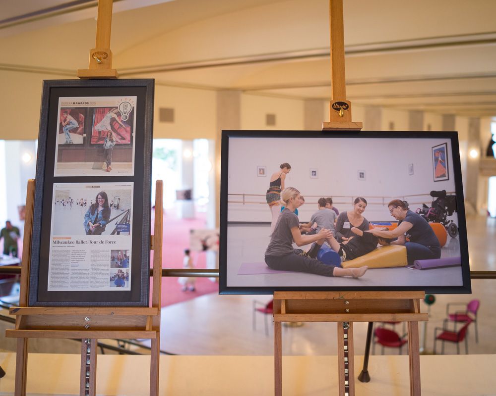 Framed photographs displayed on wooden easels in an exhibition space showing dance or performance scenes.