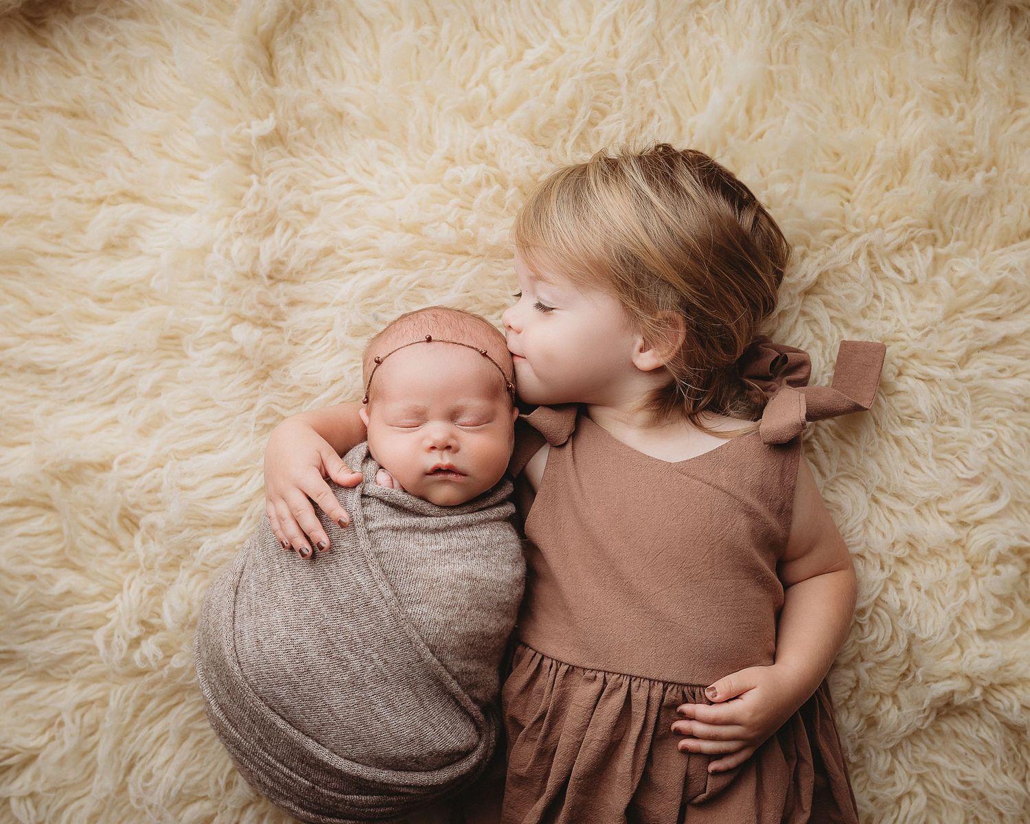 Professional photograph of a newborn baby and her big sister kissing her
