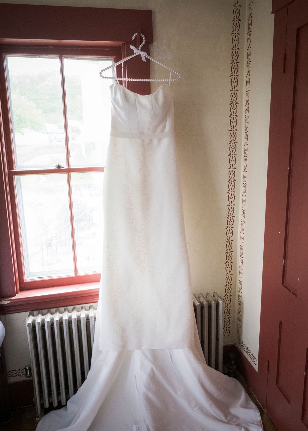 A white wedding gown hanging by a window, with soft natural light illuminating its elegant silhouette.