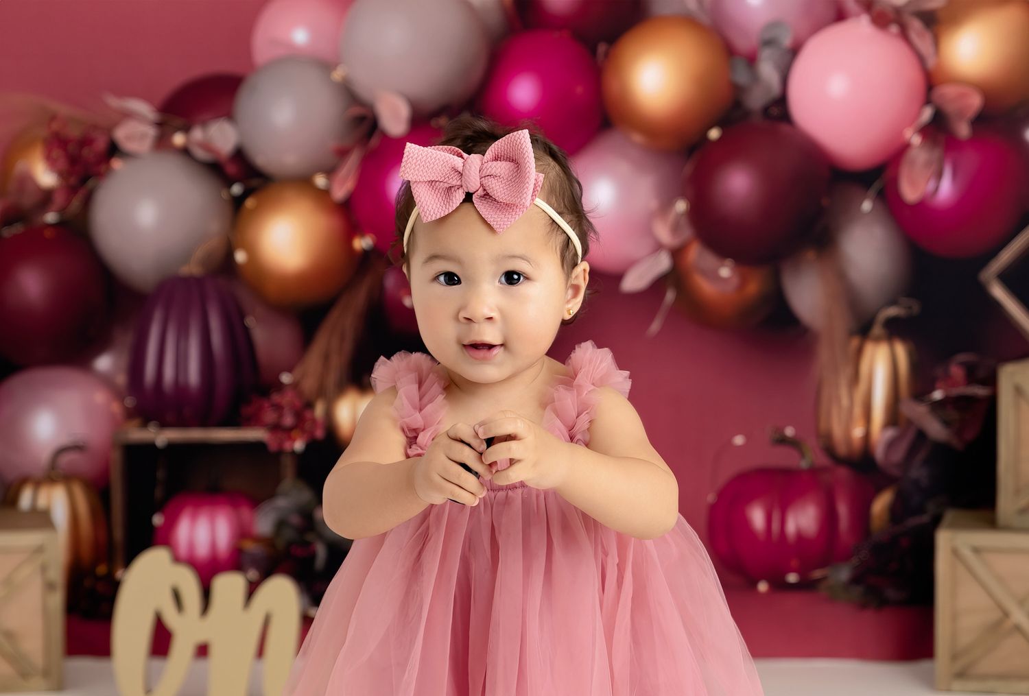 A pink tulle party dress stands out against a festive backdrop of burgundy, pink and copper balloon decorations.