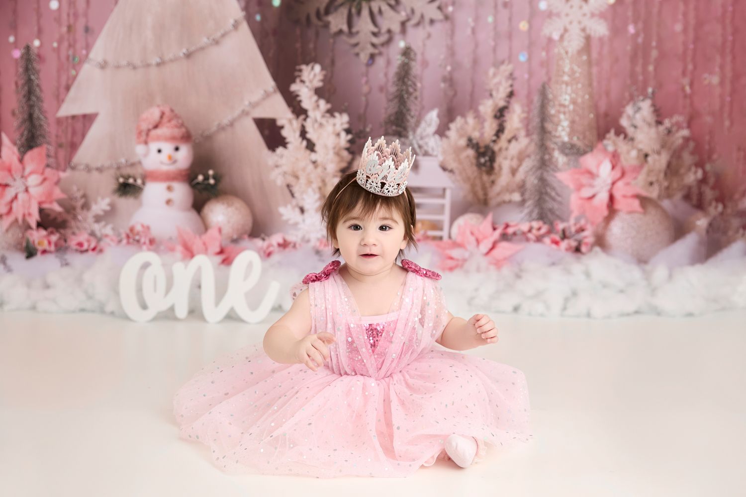 A winter wonderland photo setup with pink decor features a small figure in a pink dress among snowmen and trees.