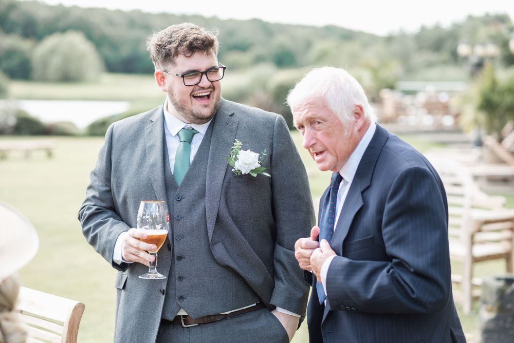 Wedding guests sharing drinks and conversation on outdoor terrace with countryside view.