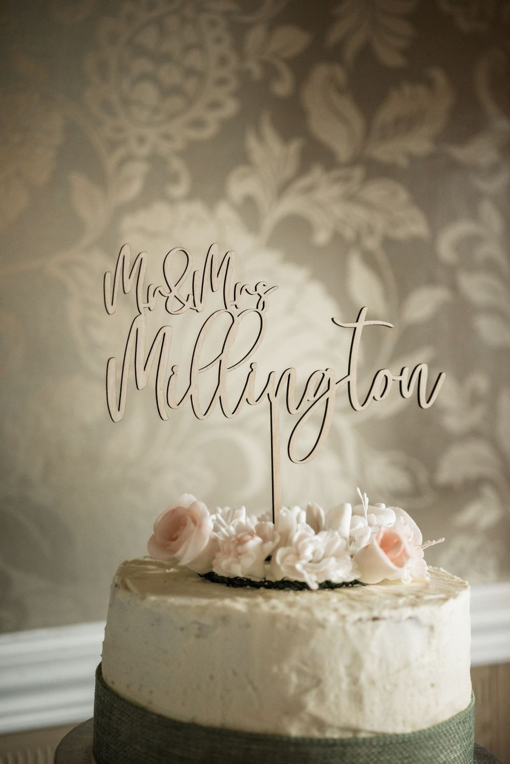 Wedding cake topper reading Mr & Mrs Millington against floral wallpaper background.