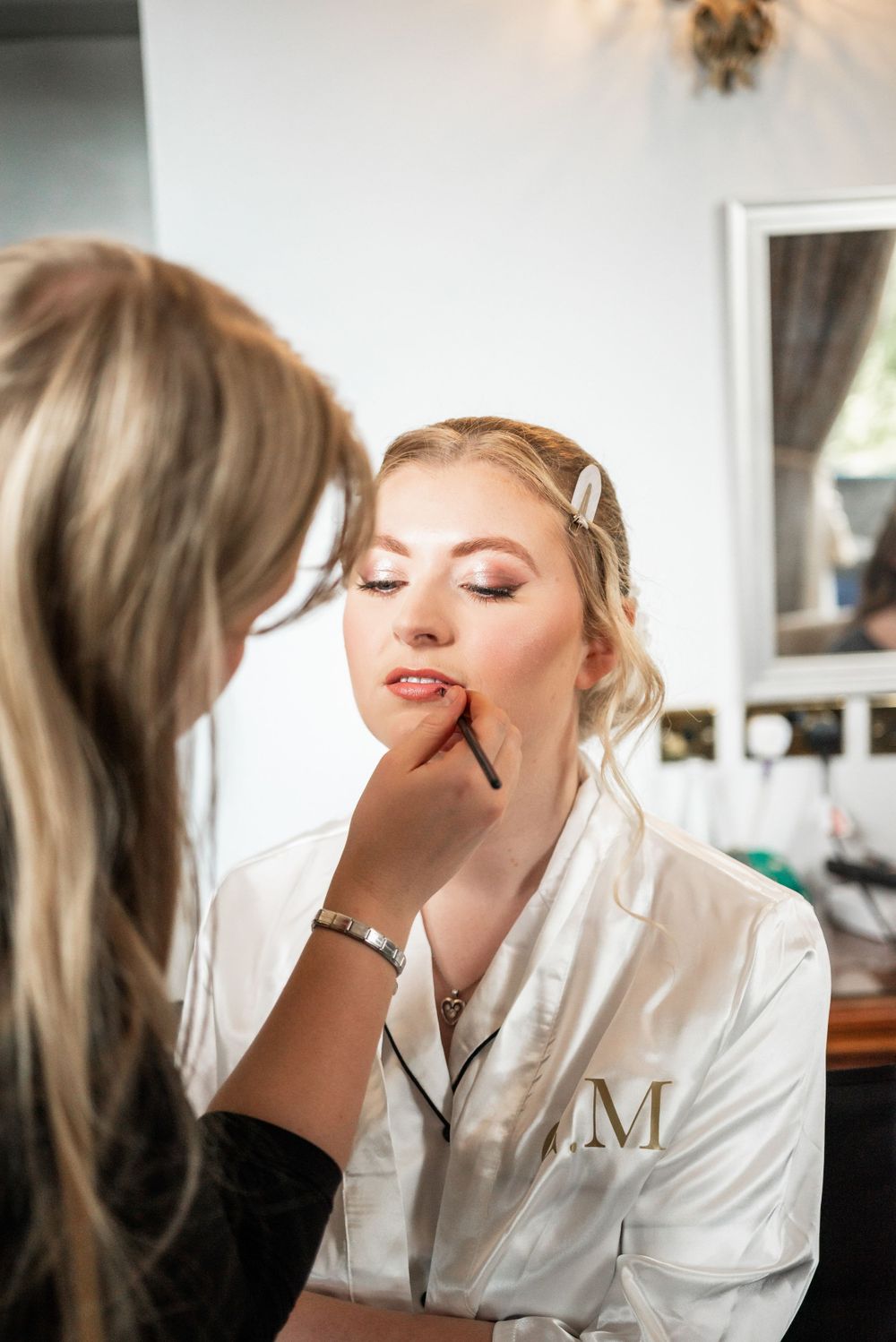 Bride getting professional makeup applied while wearing monogrammed white robe.