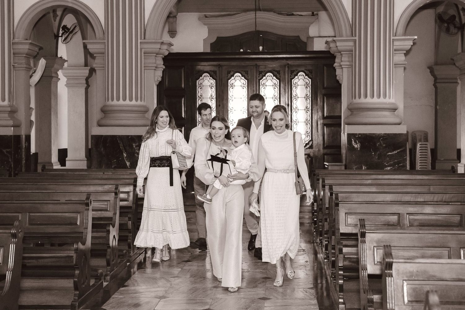 Black and white vintage photograph of a wedding party walking down the center aisle of a church with gothic arches.