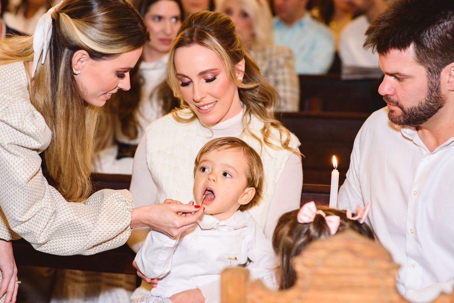 Small child opens mouth for a bite of food while sitting with adults in a restaurant setting.