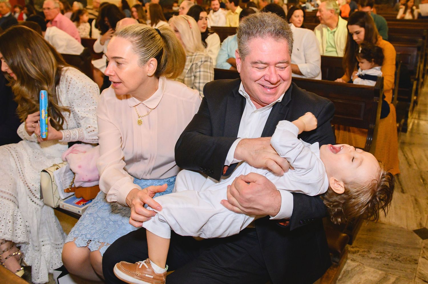 People enjoying a lively moment at a formal event as someone playfully tips another person backward in laughter.