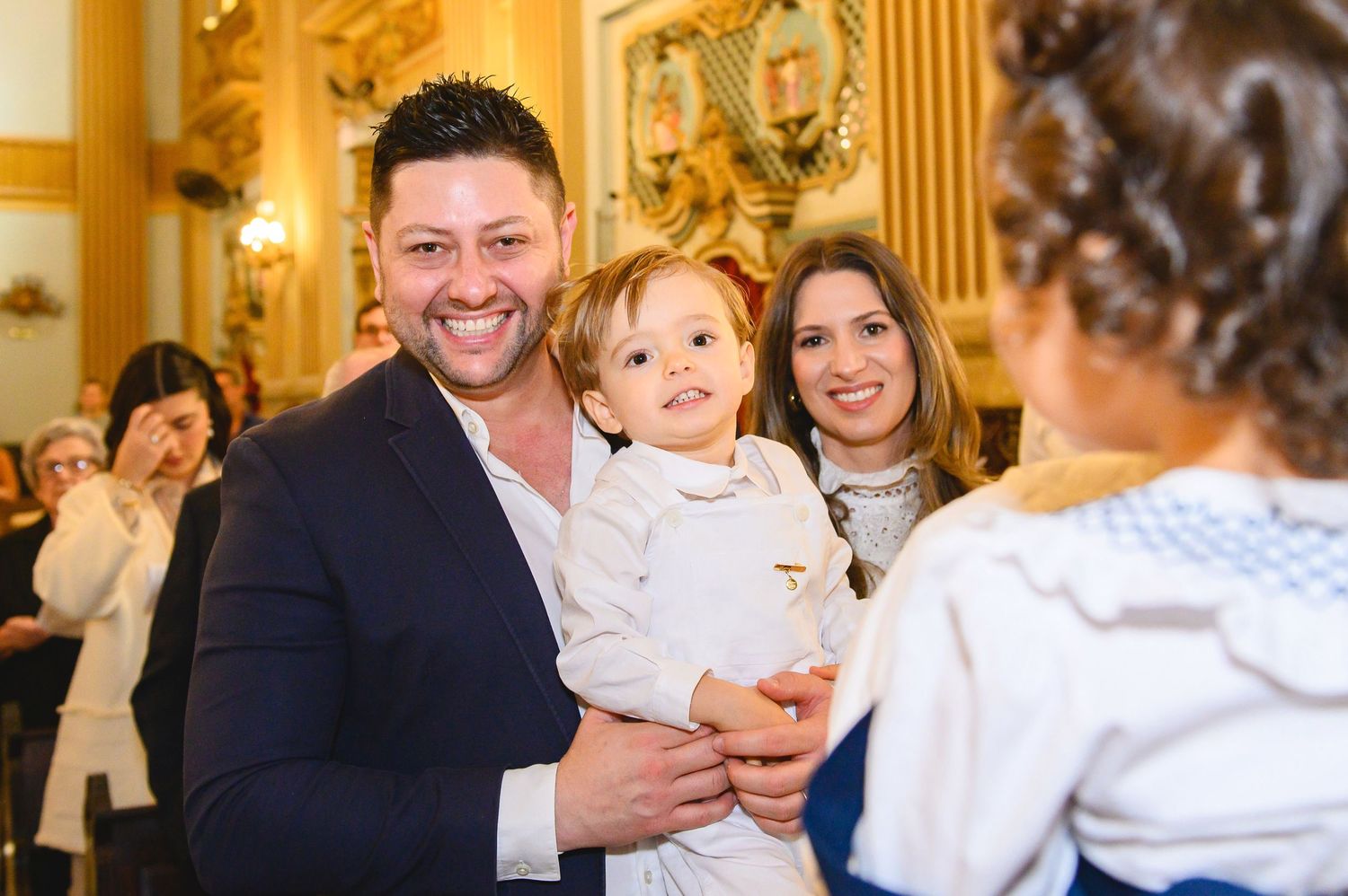 Family celebrates special occasion in elegant room with gold-toned decor and ornate details.