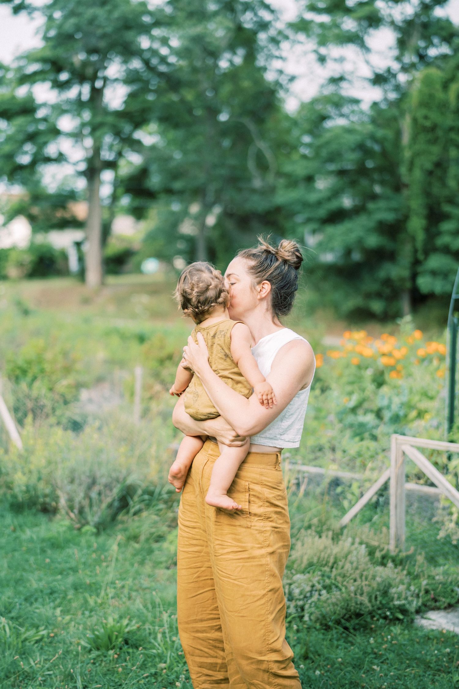 Mother and child share embrace in sunny garden with blooming flowers.