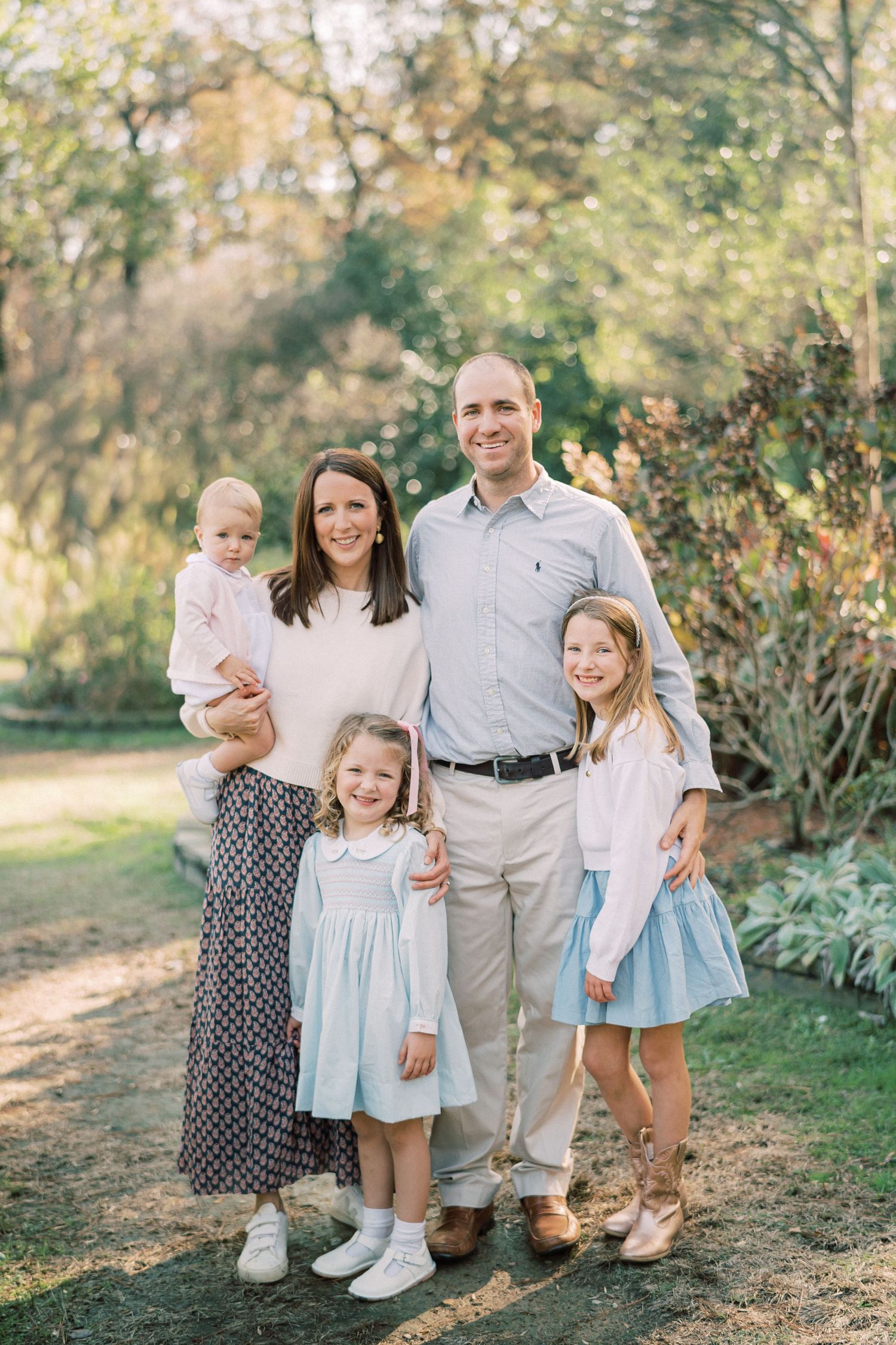 Family of five posing together on garden path with autumn foliage.
