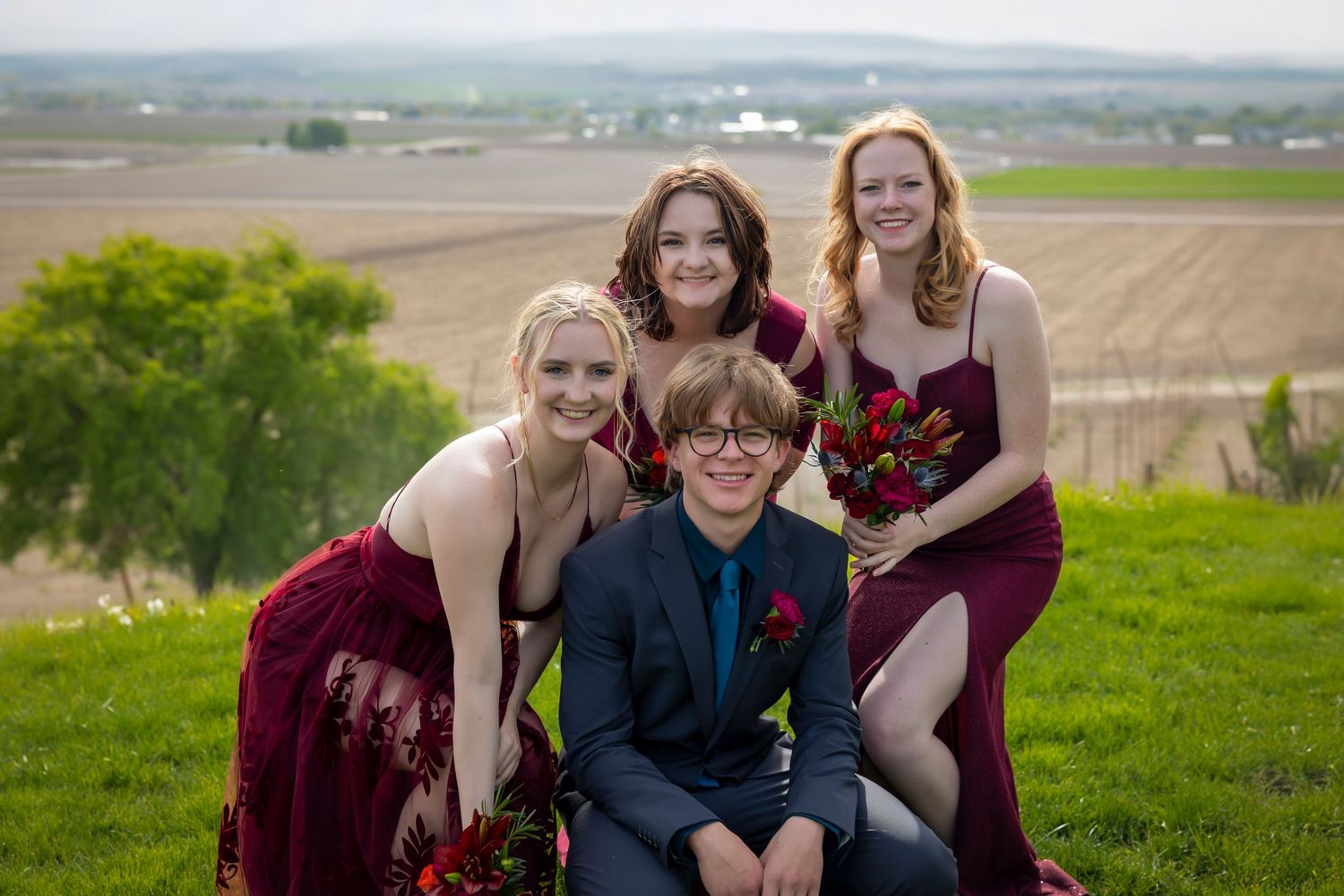 groom kneeling with 3 bridesmaids wearing burgundy
