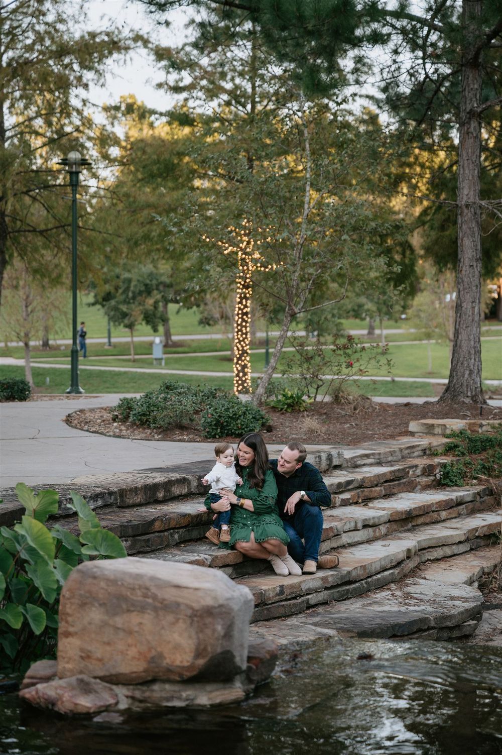 People sitting on stone steps by a pond in a park at dusk with a decorative lighted giraffe in the background.