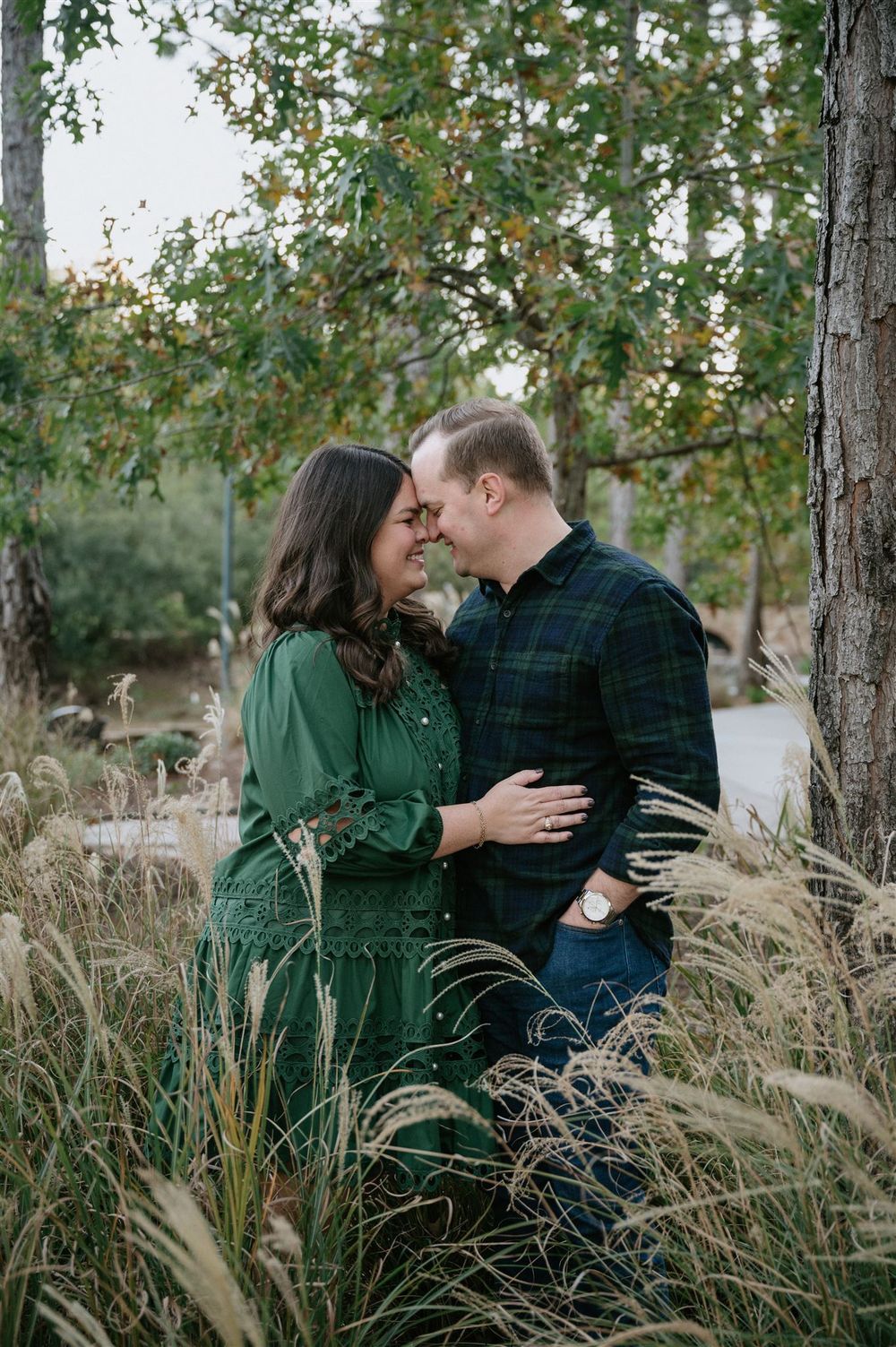 A couple shares an intimate moment among tall ornamental grasses, with the person in a green dress and other in plaid shirt.