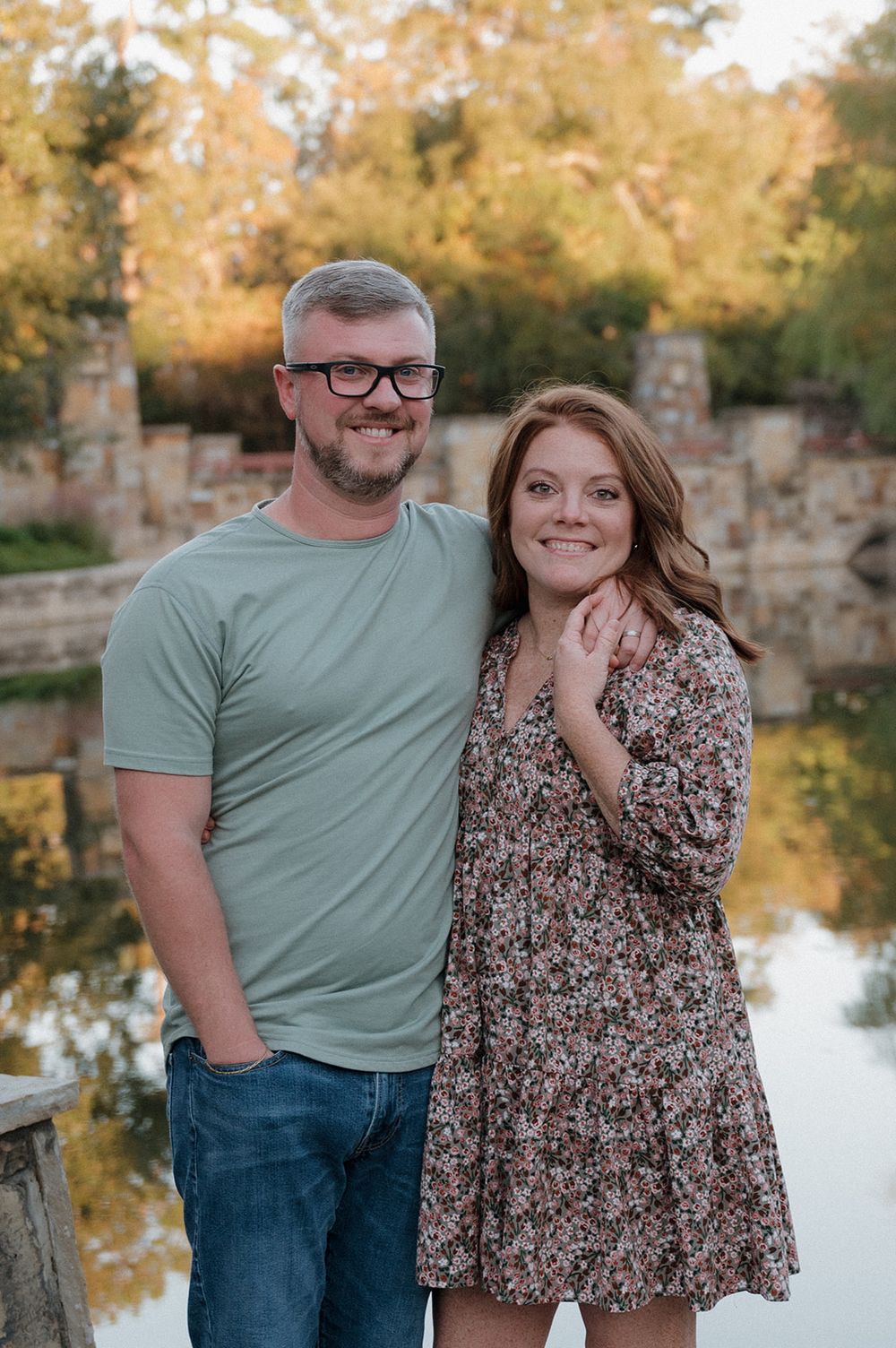 A couple poses together by a reflective pond during golden hour with stone pillars in the background.