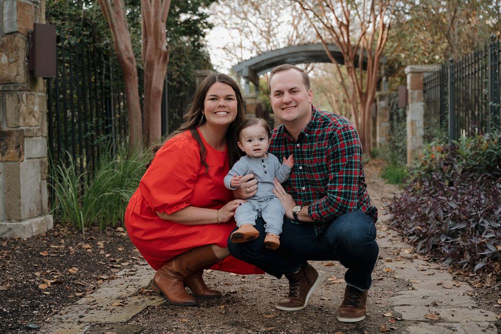 Three people pose together on a stone path surrounded by garden foliage during a family photo session.