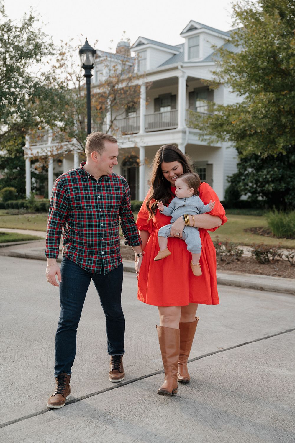 A couple walks together on a sidewalk in front of a classic Southern-style mansion with white columns and dormer windows.