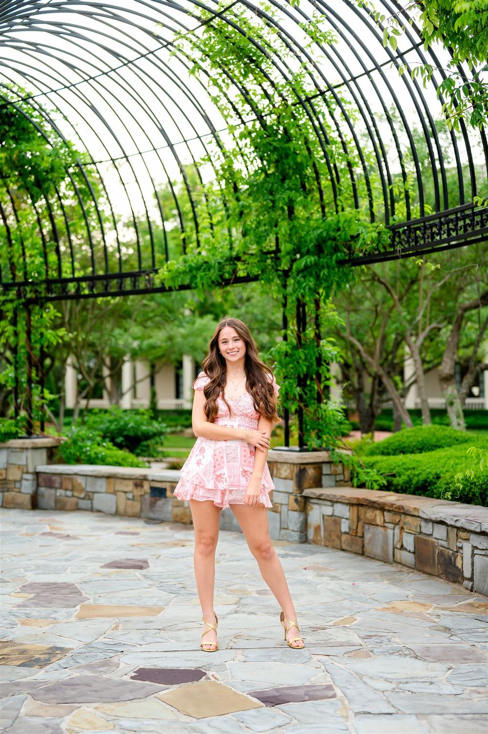 A pink lace dress brightens up a garden patio scene featuring a curved arched trellis covered in climbing greenery.