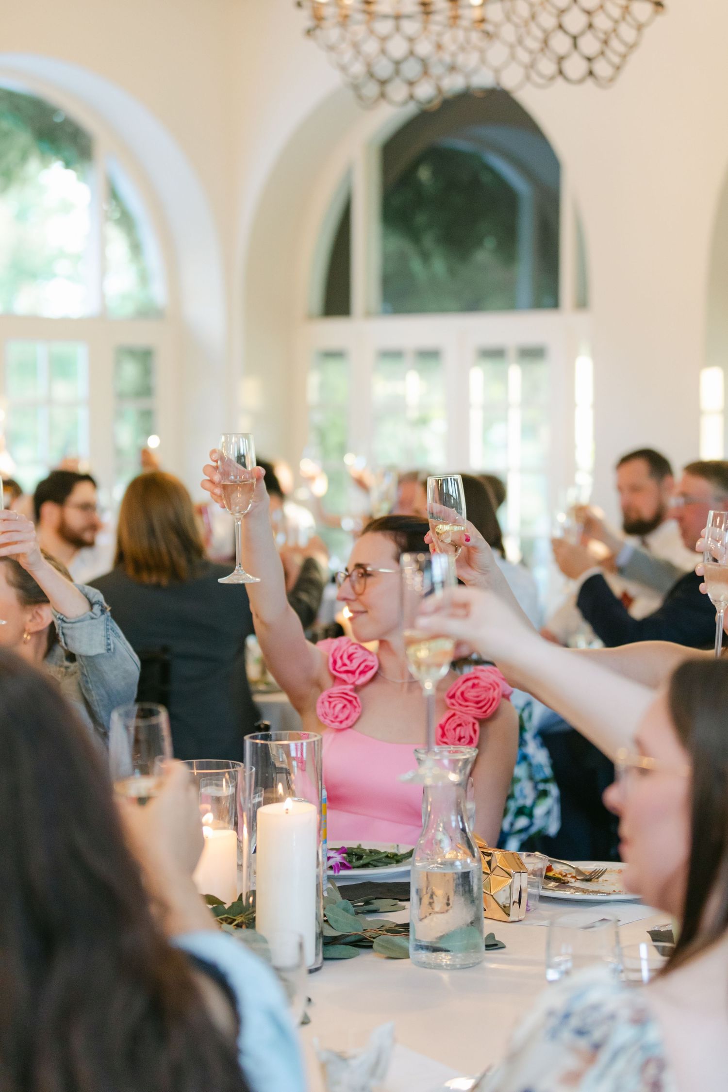People in formal attire raise champagne glasses for a toast at an elegant table decorated with greenery and white linens.