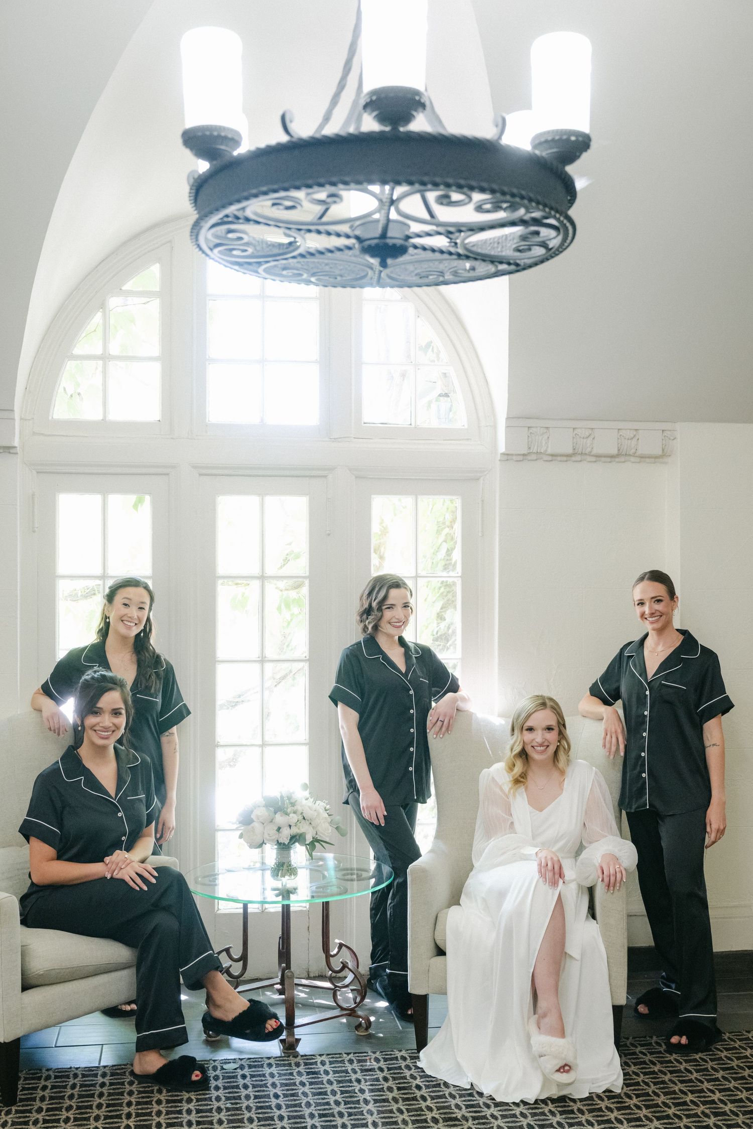 Wedding party gathered in elegant room with black and white tiled floor beneath ornate circular chandelier.