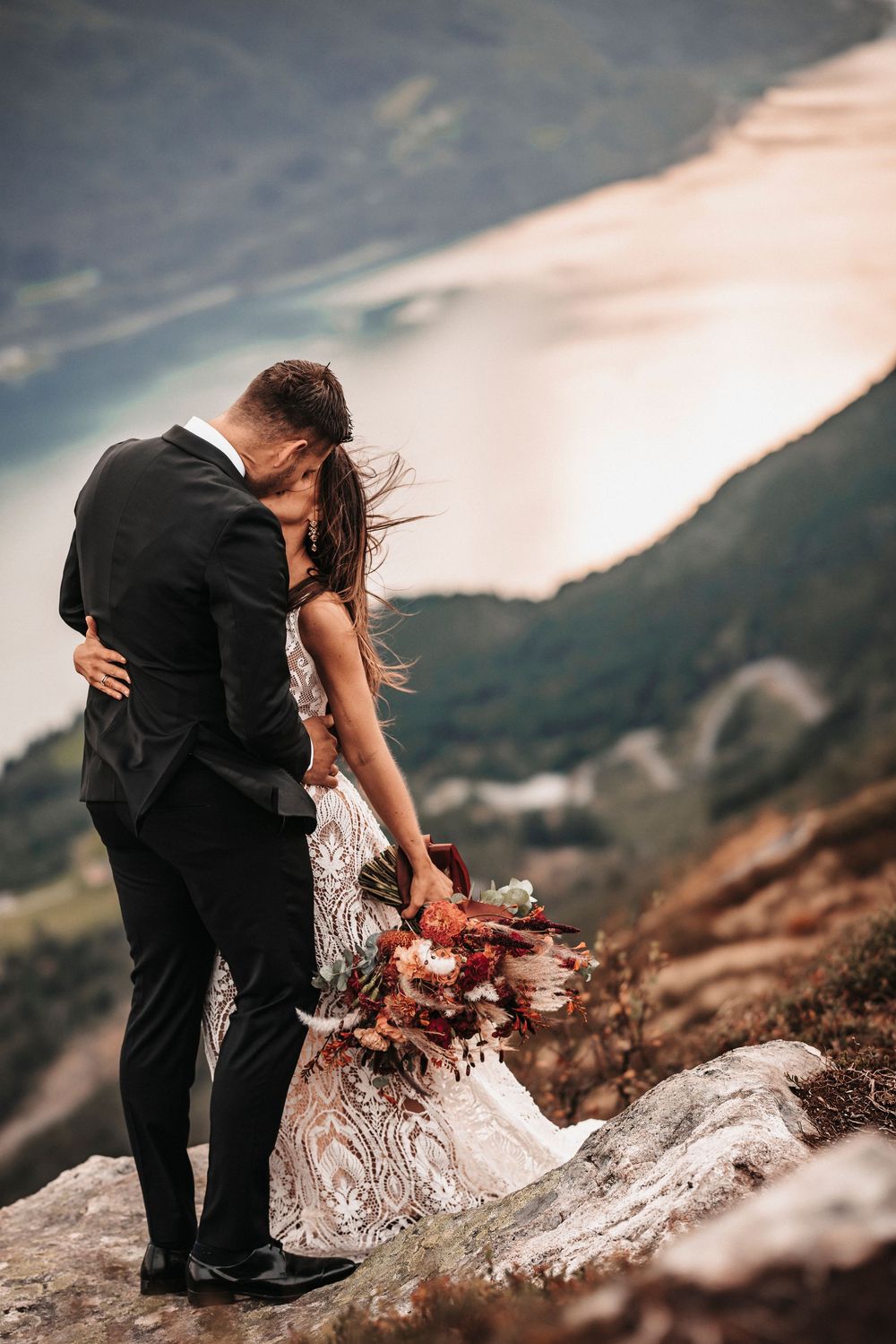 Intimate wedding moment captured on mountain ridge with dramatic landscape and flowing white dress.