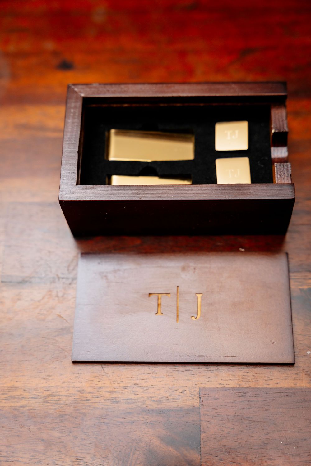 A dark wooden box with monogrammed initials T.J. containing small items is displayed on a wooden surface.