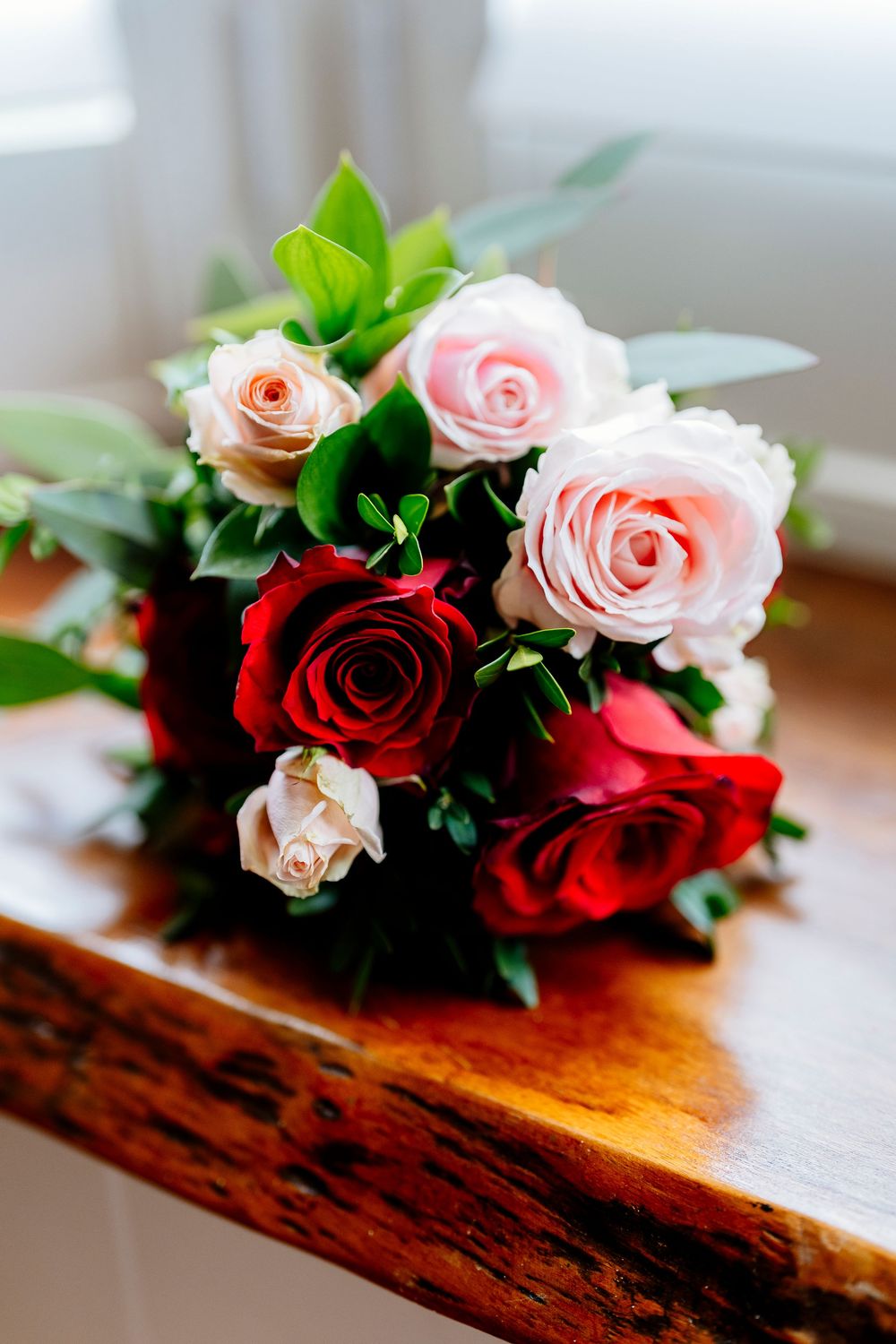 Beautiful pink and red roses arranged on a rustic wooden surface with petals and green foliage in sequence.