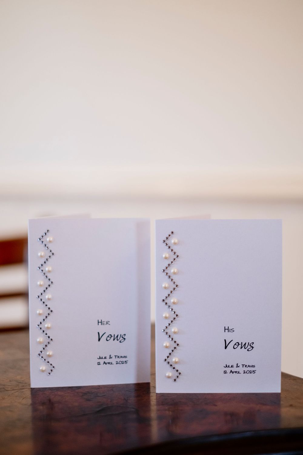 Two matching white wedding vow booklets with decorative chevron patterns displayed on a wooden surface.