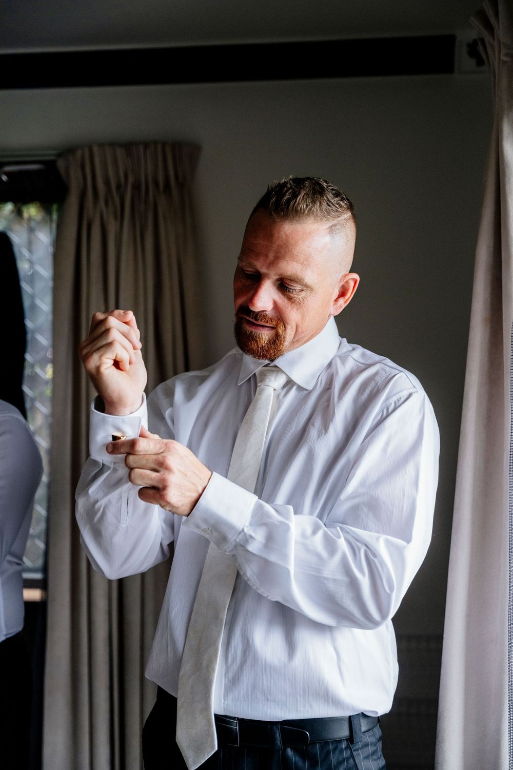 A person in a crisp white shirt and tie adjusts their cufflinks while getting ready.